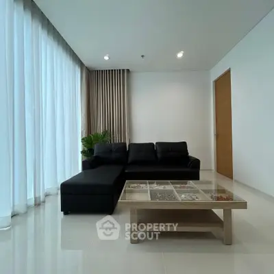 Modern living room with sleek black sofa and elegant glass coffee table, featuring floor-to-ceiling curtains.