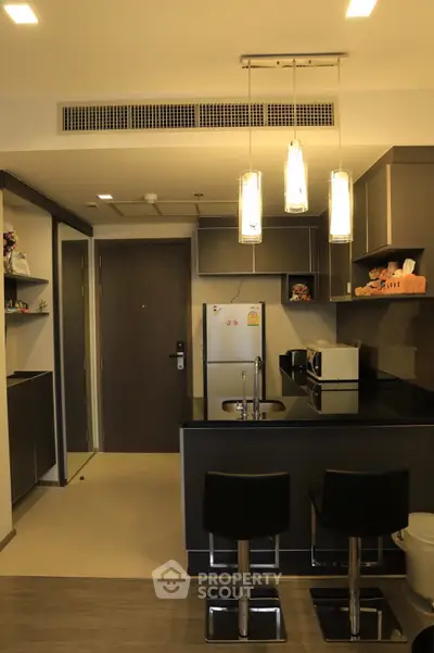 Modern kitchen with sleek black countertops and stylish bar stools in a contemporary apartment.