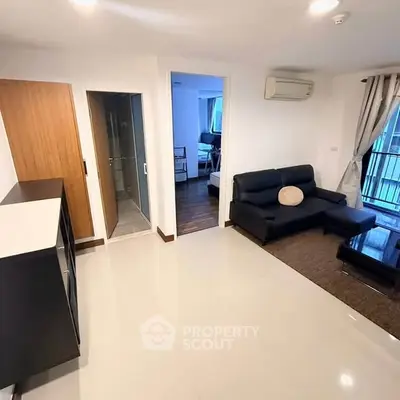 Modern living room with sleek black sofa and air conditioning, adjacent to a cozy bedroom.