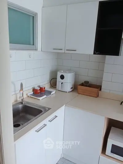 Modern kitchen with sleek white cabinets and compact appliances, perfect for efficient cooking.