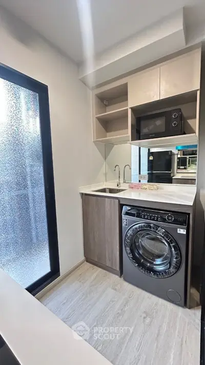 Modern compact kitchen with washing machine and microwave in sleek apartment