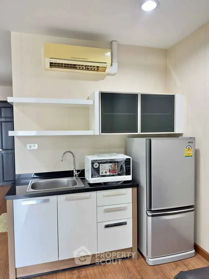 Modern compact kitchen with sleek cabinets, stainless steel fridge, and microwave in a cozy apartment.