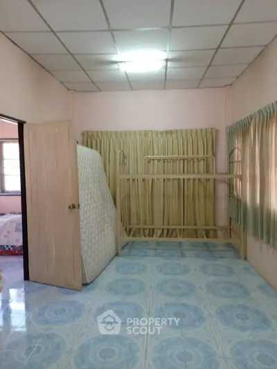 Spacious bedroom with tiled floor and ample natural light, featuring a wooden door and large windows.