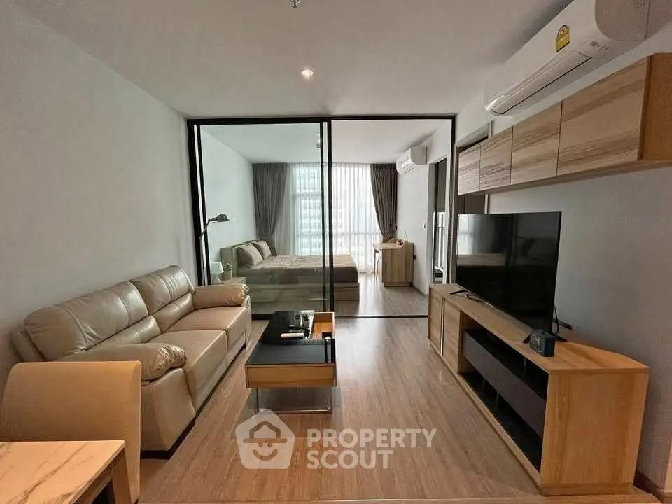 Modern open-plan living room with glass partition and cozy bedroom view.