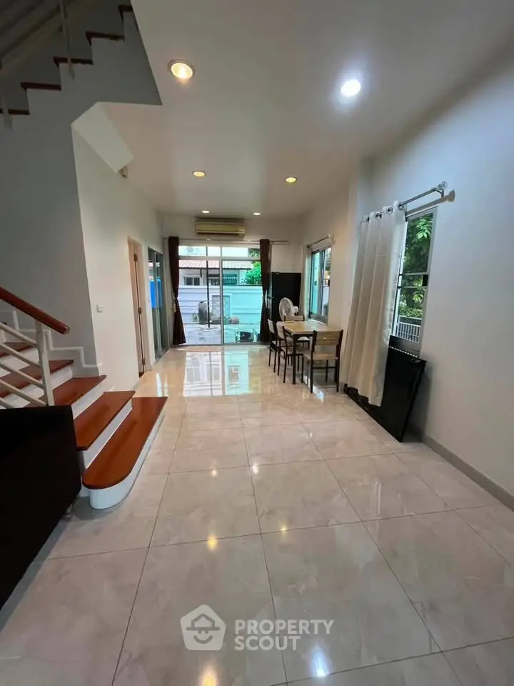 Spacious open-plan living area with modern staircase and dining space, featuring large windows for natural light.