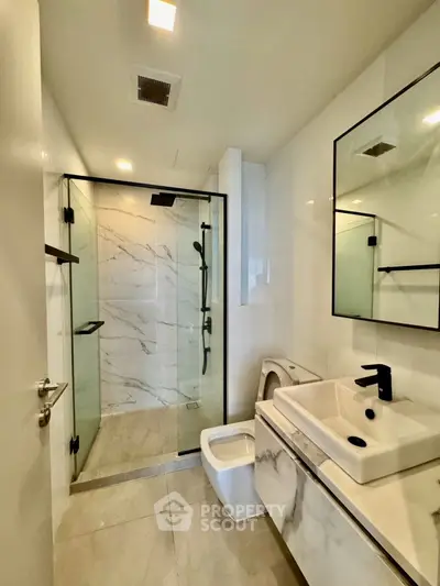 Modern bathroom with glass shower and sleek fixtures in luxury apartment.