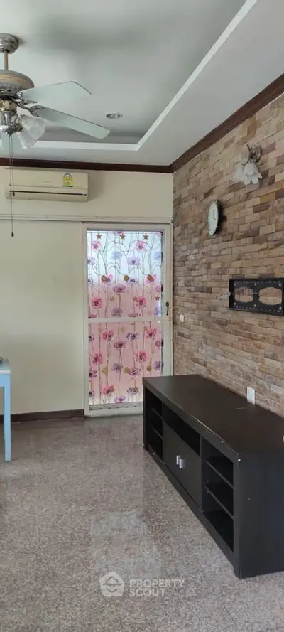 Charming living room with brick accent wall and floral door design, featuring ceiling fan and air conditioning.
