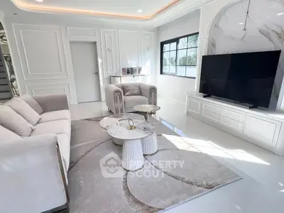 Luxurious modern living room with elegant furniture and large TV, featuring natural light and stylish decor.