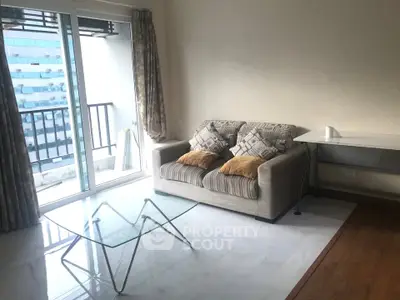 Bright living room with modern sofa, glass coffee table, and balcony view in urban apartment.