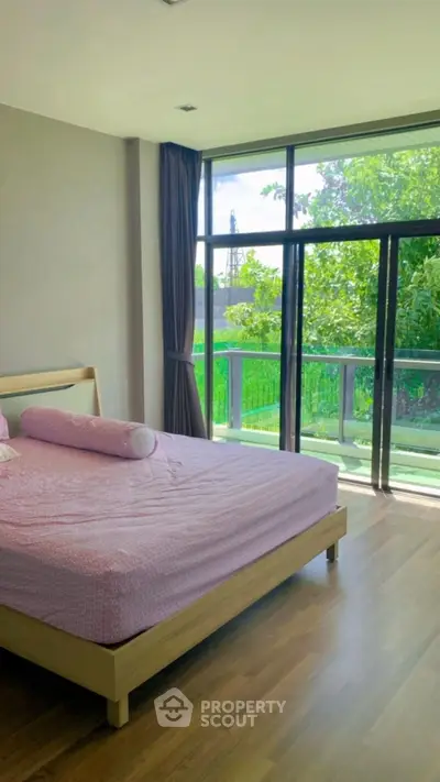 Spacious bedroom with large windows and balcony overlooking greenery