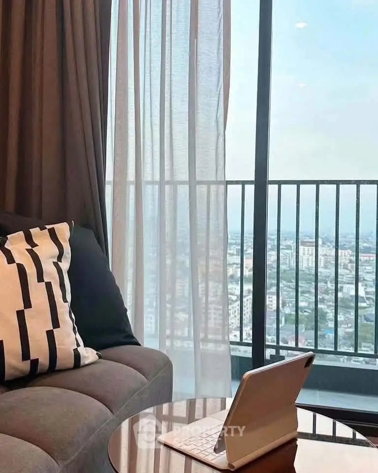 Modern living room with stunning city view from balcony, featuring cozy sofa and tablet on table.