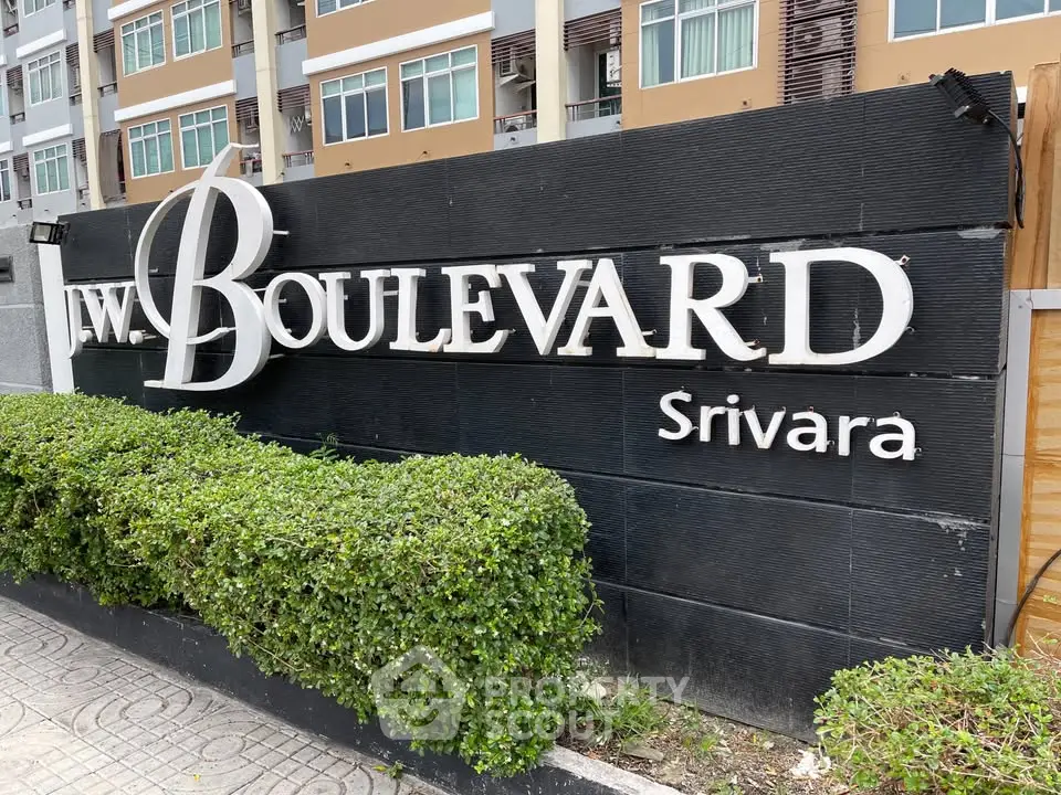 Modern apartment building entrance with stylish signage and lush greenery.