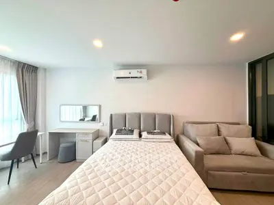 Modern bedroom with stylish decor, featuring a cozy bed, sofa, and workspace under natural light.