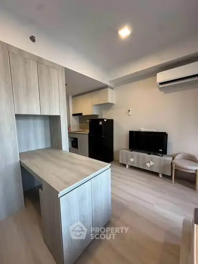 Modern living room with sleek wooden furniture and built-in storage, featuring a compact kitchen area.
