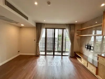 Spacious living room with wooden flooring and balcony access in modern apartment.