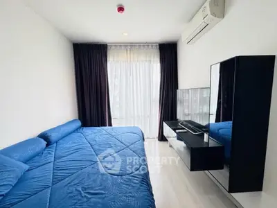 Modern bedroom with blue bedding, wall-mounted TV, and large window with curtains.