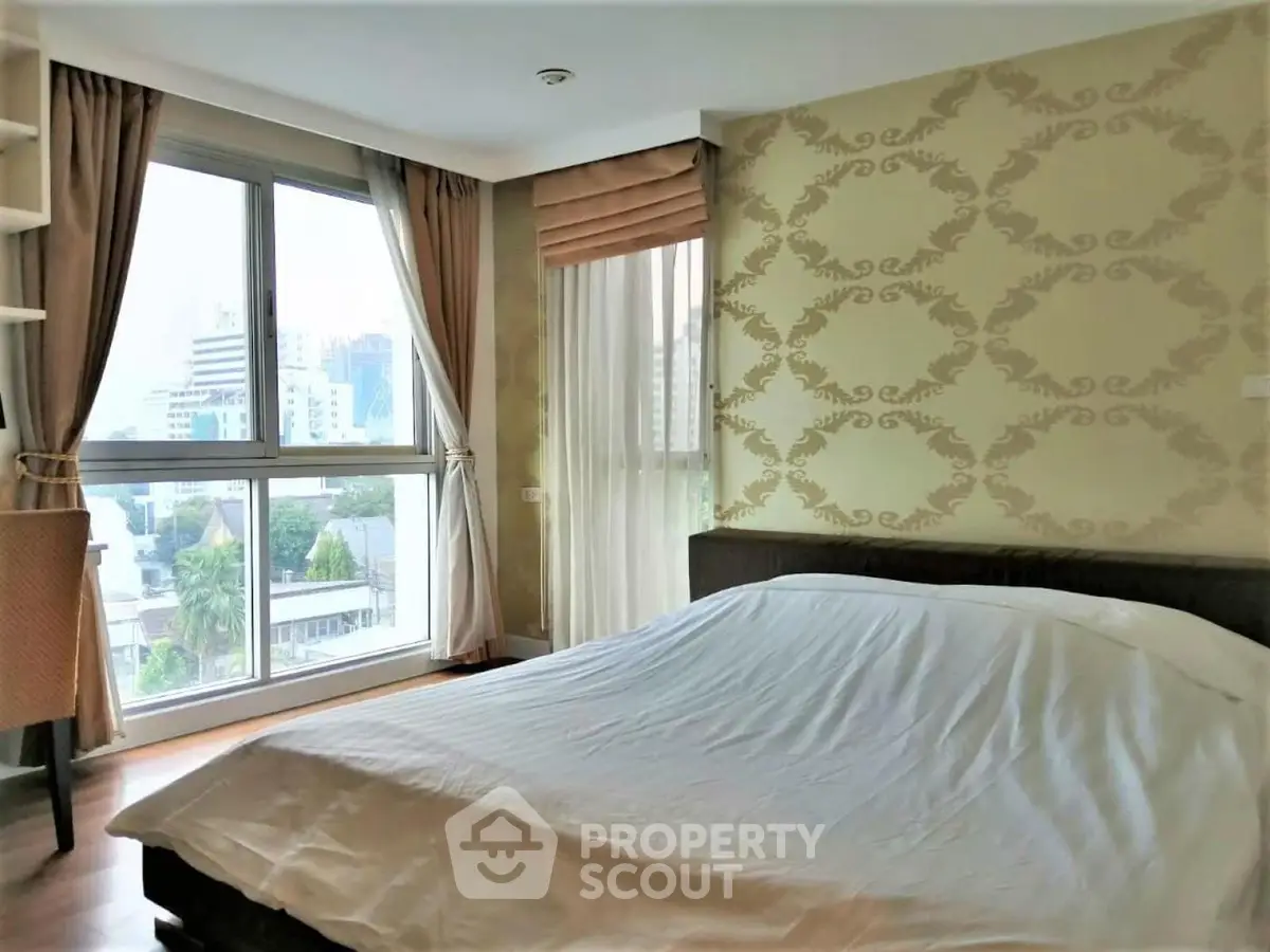 Spacious bedroom with large windows offering city views and elegant wallpaper design.