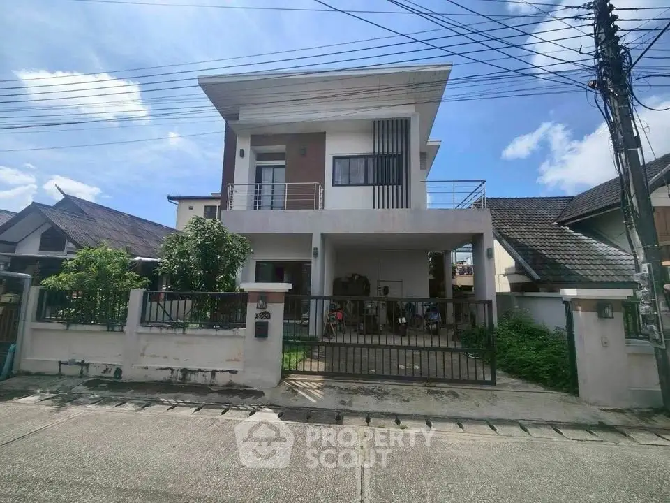 Modern two-story house with balcony and gated driveway in a suburban neighborhood.