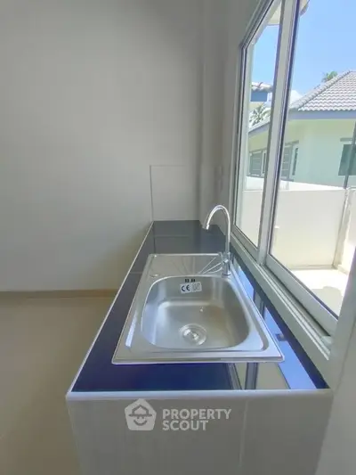 Modern kitchen with sleek countertop and stainless steel sink, bright natural light from large window.