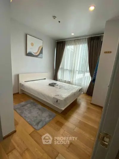 Modern bedroom with wooden flooring, large window, and stylish decor in a cozy apartment.