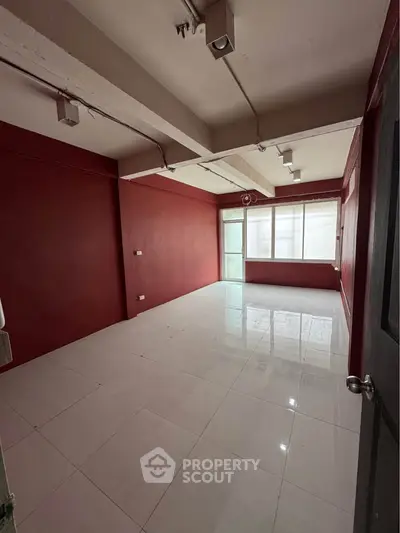 Spacious empty room with red walls and large window, ideal for customization.