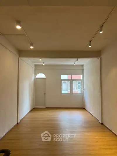Spacious empty room with wooden flooring and ample natural light, ideal for customization.
