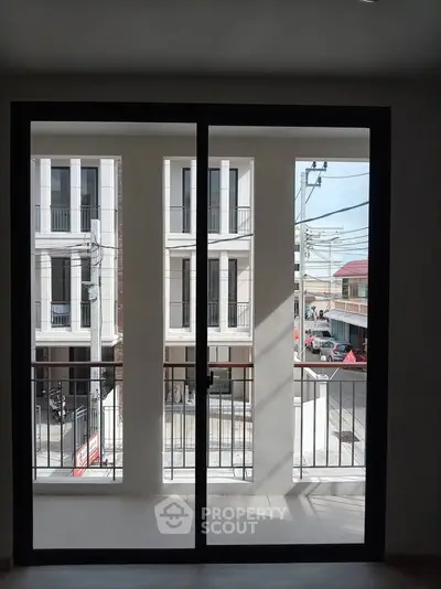 Modern apartment balcony with city view, showcasing sleek glass doors and urban surroundings.