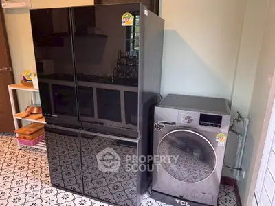 Modern kitchen with sleek black fridge and advanced washing machine on patterned floor.