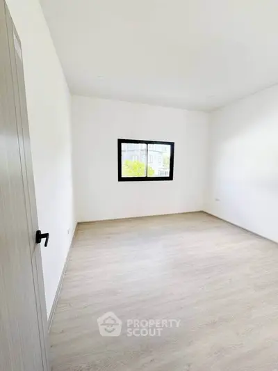 Spacious empty room with large window and light wood flooring, perfect for customization.