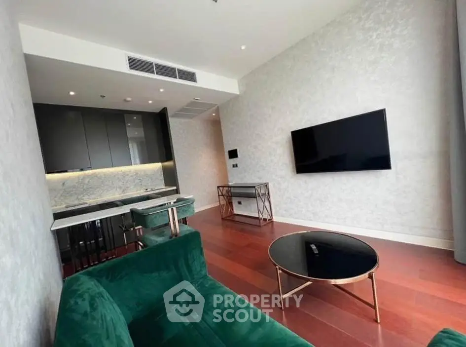 Modern living room with elegant green sofa, sleek TV, and stylish kitchen area in open layout.