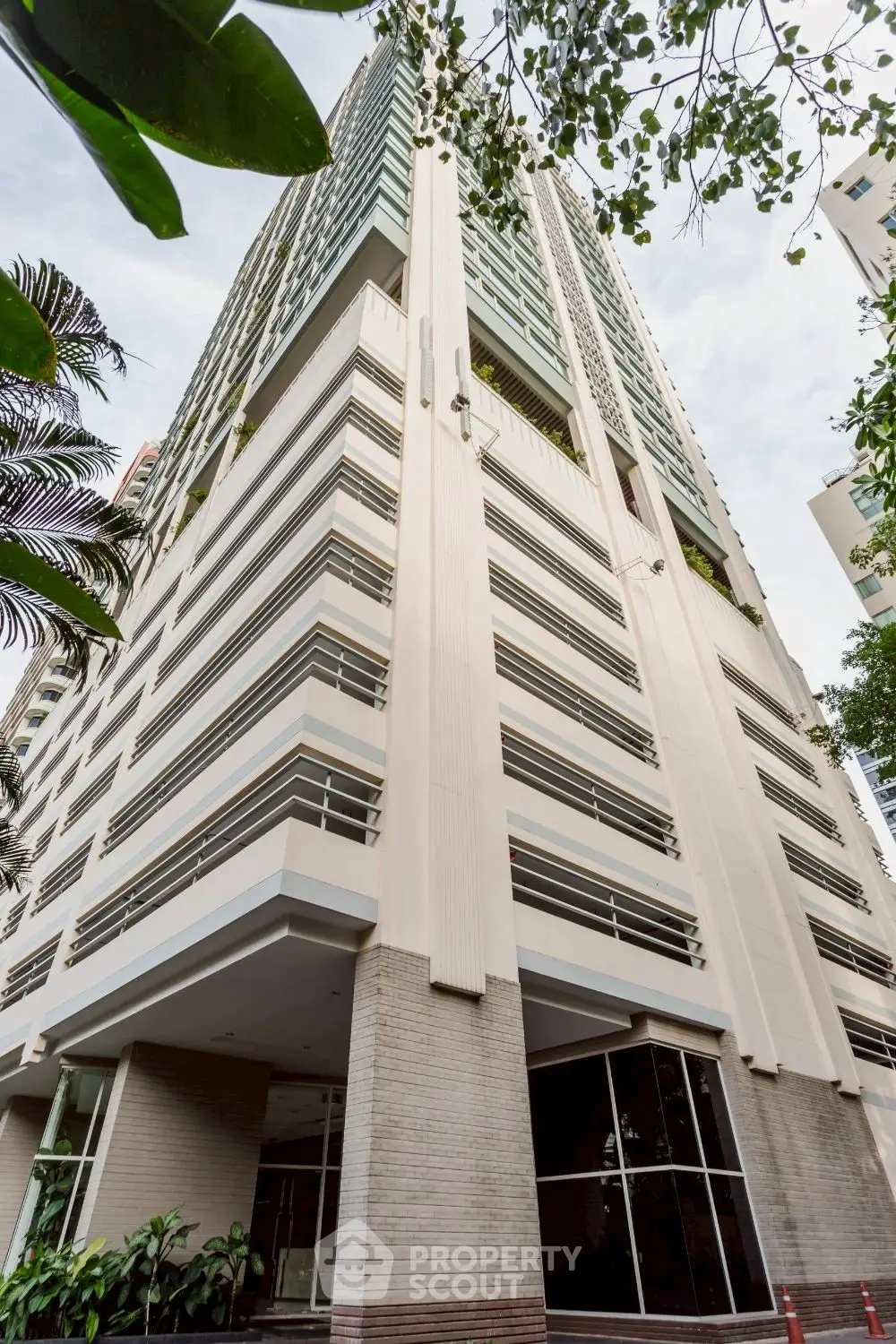 Modern high-rise building with sleek architecture and lush greenery in urban setting.