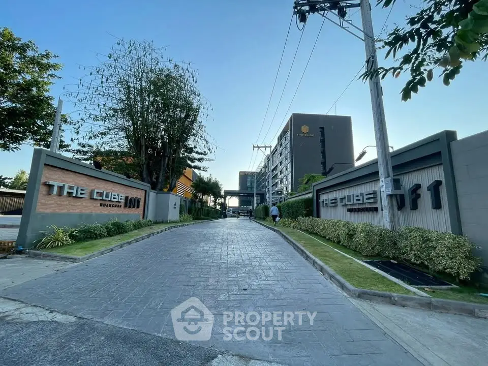 Modern residential building entrance with lush greenery and clear sky, showcasing urban living.