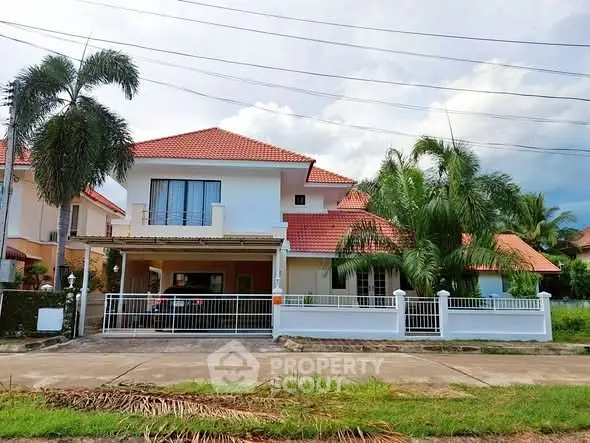 Charming two-story house with red-tiled roof and lush palm trees in a serene neighborhood.