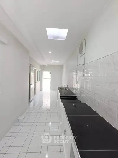 Spacious kitchen with sleek black countertops and white tiled flooring, featuring a modern open layout.