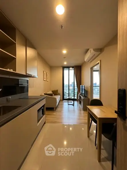 Modern open-plan living room with kitchen and city view, featuring sleek furniture and natural light.