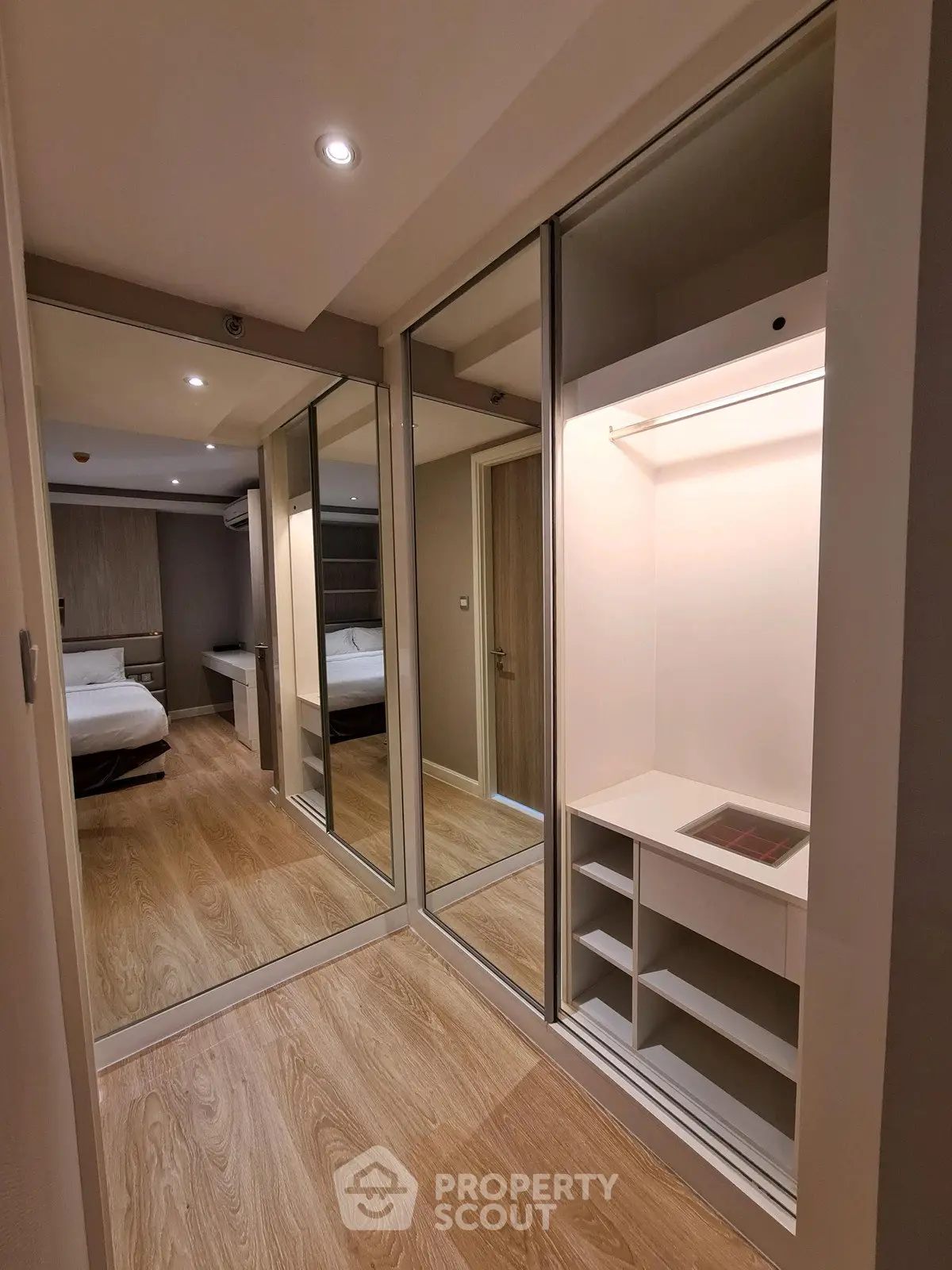 Spacious bedroom with mirrored closet doors and wooden flooring in modern apartment.