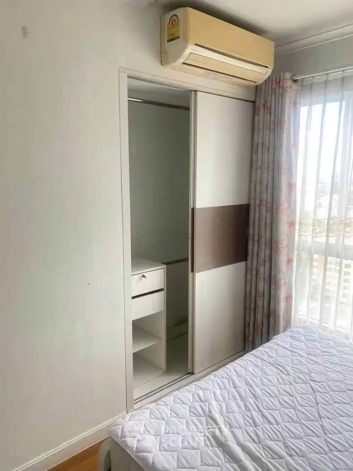 Cozy bedroom with built-in wardrobe and air conditioning, featuring a large window with floral curtains.