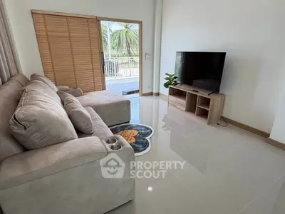 Spacious living room with modern sofa and large TV, opening to a balcony with a scenic view.
