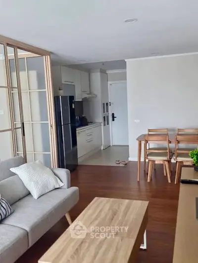 Modern open-plan living room with sleek kitchen and dining area, featuring stylish furniture and wooden flooring.