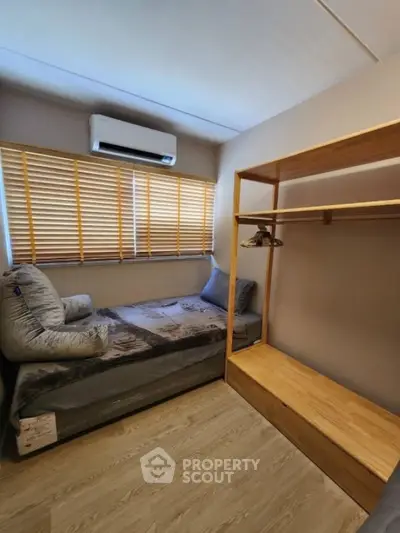 Cozy bedroom with wooden flooring and open wardrobe, featuring a single bed and air conditioning.