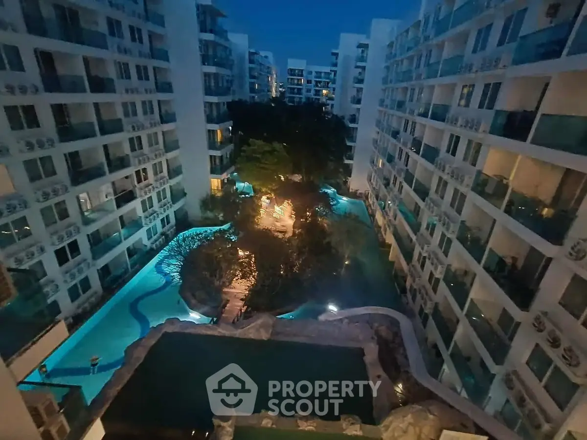 Stunning night view of modern apartment complex with illuminated pool and lush garden.