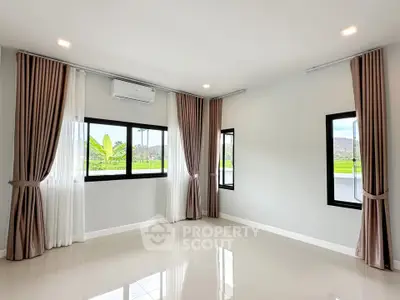 Spacious empty room with large windows and elegant curtains, offering a serene view.