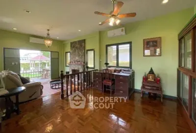 Charming living room with wooden floors and ceiling fan, opening to a spacious balcony with garden view.