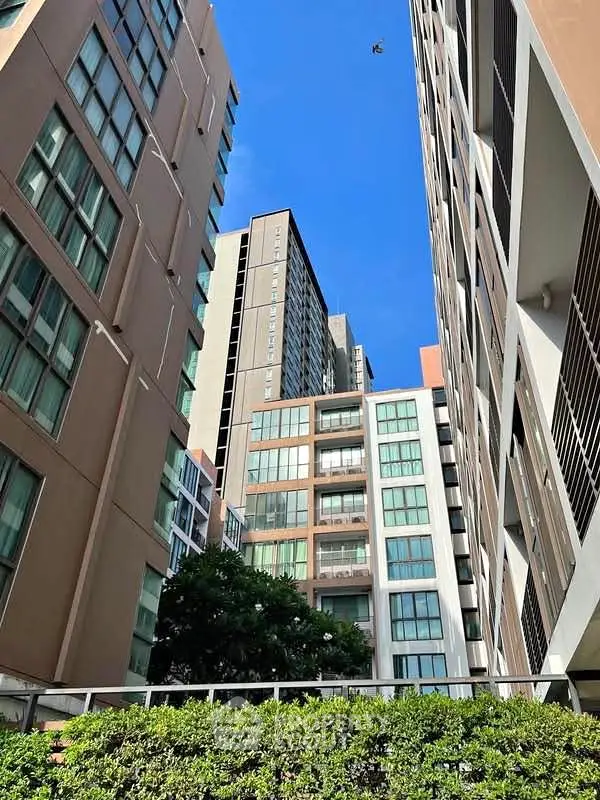Modern urban apartment buildings with lush greenery and clear blue sky.