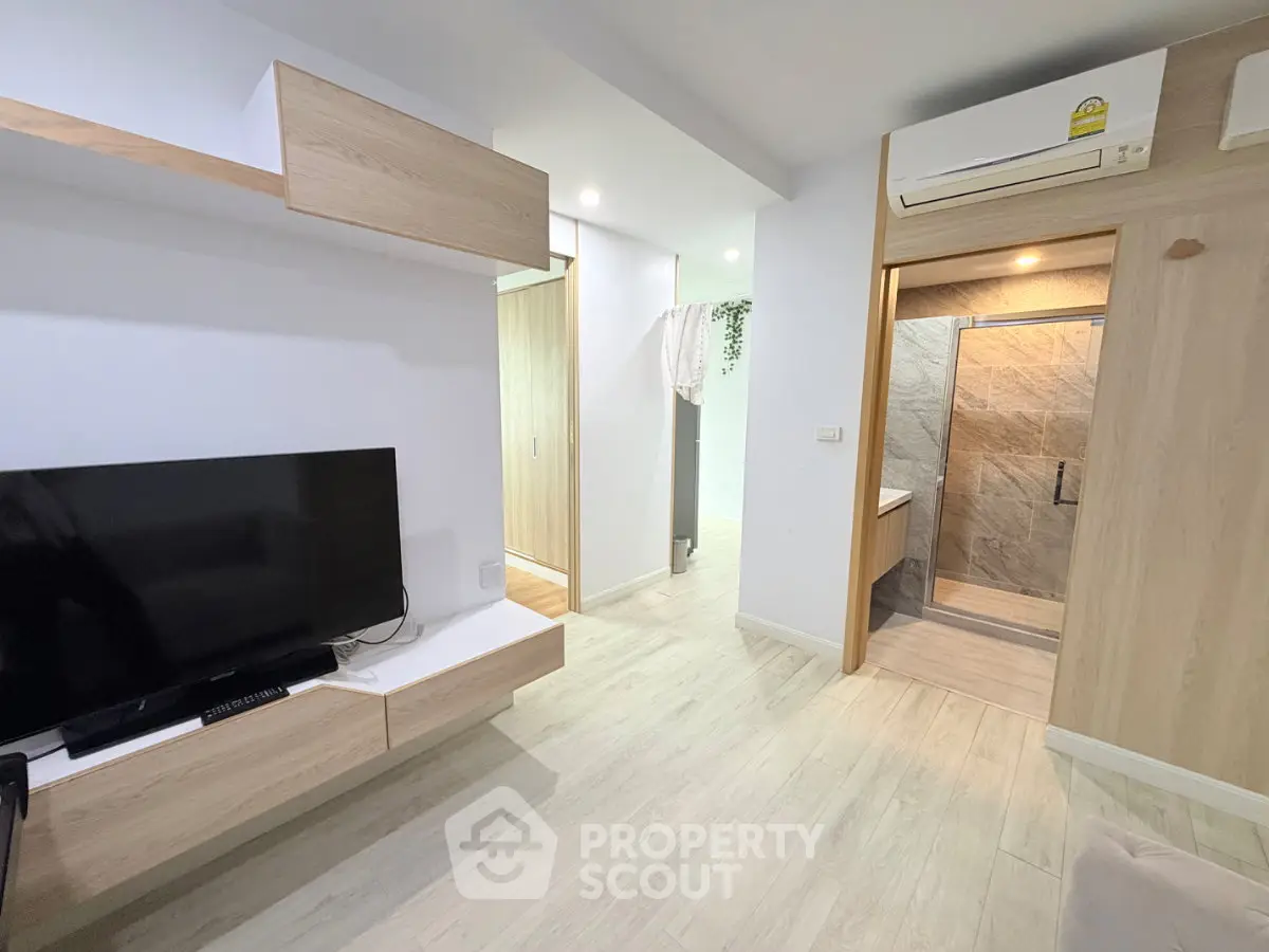 Modern living room with sleek wooden furniture and wall-mounted TV, adjacent to a stylish bathroom.