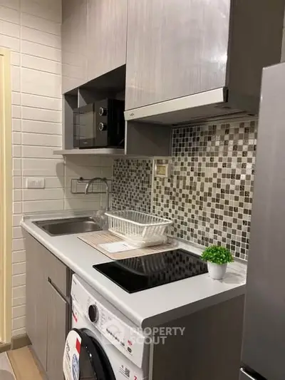 Modern compact kitchen with sleek cabinetry, mosaic backsplash, and built-in appliances for efficient living.