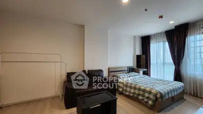 Spacious studio apartment with cozy bed and leather sofa, featuring large windows for natural light.