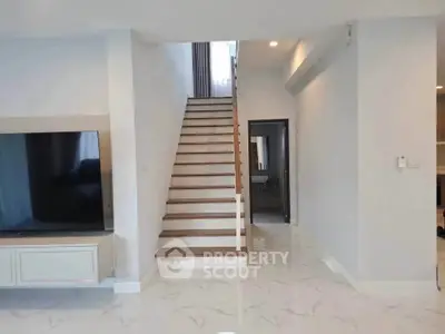 Modern interior with sleek staircase and spacious living area featuring a large TV setup.