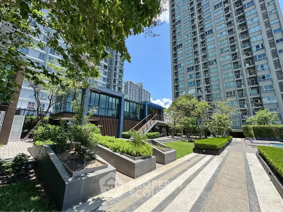 Modern high-rise residential building with lush landscaped garden and clear blue sky.