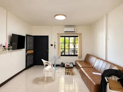 Spacious living room with modern decor and natural light, featuring a leather sofa and wall-mounted TV.